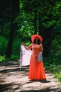 Adult woman in a long coral dress and a wide hat walks in a summer park