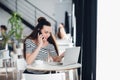 Beautiful adult woman in striped shirt is talking on the phone, holding a cup and smiling while working with a laptop in Royalty Free Stock Photo