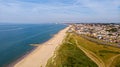 A beautiful aerial seaside view with sandy beach, crystal blue water, groynes breakwaters and green vegetation dunes along a