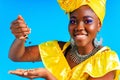 beautiful africa-american woman with yellow turban ower the head showing fresh coffee beand in studio blue baclground