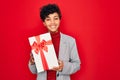 Beautiful african american afro business woman holding gift over isolated red background with a happy face standing and smiling Royalty Free Stock Photo