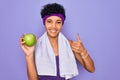 Beautiful african american afro sporty woman doing exercise wearing towel eating green apple happy with big smile doing ok sign, Royalty Free Stock Photo