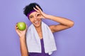 Beautiful african american afro sporty woman doing exercise wearing towel eating green apple with happy face smiling doing ok sign Royalty Free Stock Photo