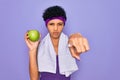 Beautiful african american afro sporty woman doing exercise wearing towel eating green apple pointing with finger to the camera Royalty Free Stock Photo