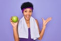 Beautiful african american afro sporty woman doing exercise wearing towel eating green apple very happy and excited, winner Royalty Free Stock Photo