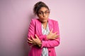 Beautiful african american businesswoman wearing jacket and glasses over pink background shaking and freezing for winter cold with