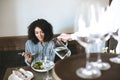 Beautiful African American girl sitting in restaurant and eating salad while waiter pouring water in glass Portrait of Royalty Free Stock Photo