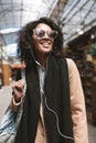 Beautiful African American girl standing on street in earphones. Portrait of cool girl with dark curly hair in Royalty Free Stock Photo