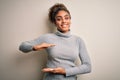 Beautiful african american girl wearing turtleneck sweater standing over white background gesturing with hands showing big and Royalty Free Stock Photo