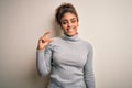 Beautiful african american girl wearing turtleneck sweater standing over white background smiling and confident gesturing with Royalty Free Stock Photo