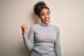 Beautiful african american girl wearing turtleneck sweater standing over white background smiling with happy face looking and Royalty Free Stock Photo