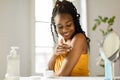 Beautiful african american lady applying cream on her shoulder, taking care of skin after bath in bedroom, free space Royalty Free Stock Photo