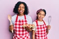 Beautiful african american mother and daughter cooking cake using baker whisk winking looking at the camera with sexy expression,