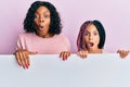 Beautiful african american mother and daughter holding blank empty banner scared and amazed with open mouth for surprise,