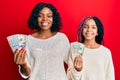 Beautiful african american mother and daughter holding dollars looking positive and happy standing and smiling with a confident Royalty Free Stock Photo