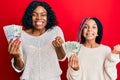 Beautiful african american mother and daughter holding dollars screaming proud, celebrating victory and success very excited with Royalty Free Stock Photo