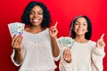 Beautiful african american mother and daughter holding dollars smiling happy pointing with hand and finger to the side Royalty Free Stock Photo