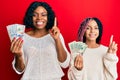 Beautiful african american mother and daughter holding dollars smiling with an idea or question pointing finger with happy face, Royalty Free Stock Photo