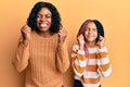 Beautiful african american mother and daughter wearing wool winter sweater excited for success with arms raised and eyes closed Royalty Free Stock Photo