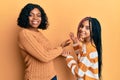 Beautiful african american mother and daughter wearing wool winter sweater inviting to enter smiling natural with open hand Royalty Free Stock Photo