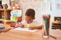 Beautiful african american toddler sitting drawing using paper and pencils on desk at kindergarten Royalty Free Stock Photo