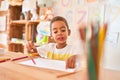 Beautiful african american toddler sitting drawing using paper and pencils on desk at kindergarten Royalty Free Stock Photo