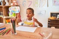 Beautiful african american toddler sitting drawing using paper and pencils on desk at kindergarten Royalty Free Stock Photo