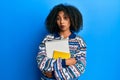 Beautiful african american woman with afro hair holding books clueless and confused expression Royalty Free Stock Photo