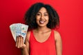 Beautiful african american woman with afro hair holding dollars looking positive and happy standing and smiling with a confident Royalty Free Stock Photo