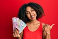 Beautiful african american woman with afro hair holding indian rupee banknotes pointing thumb up to the side smiling happy with Royalty Free Stock Photo