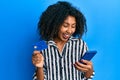 Beautiful african american woman with afro hair holding smartphone and credit card smiling and laughing hard out loud because Royalty Free Stock Photo