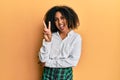 Beautiful african american woman with afro hair wearing scholar skirt smiling with happy face winking at the camera doing victory Royalty Free Stock Photo