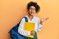 Beautiful african american woman with afro hair wearing school bag and holding books celebrating victory with happy smile and Royalty Free Stock Photo