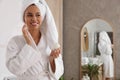 Beautiful African American woman applying cream onto face in bathroom, space for text Royalty Free Stock Photo