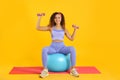 Beautiful African American woman doing exercise with fitness ball and dumbbells on yoga mat against yellow background Royalty Free Stock Photo