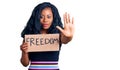 Beautiful african american woman holding freedom banner with open hand doing stop sign with serious and confident expression,