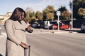 Beautiful African American woman holding suitcase and looking at wristwatch. Holiday and travel concept