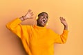 Beautiful african american young woman with short hair wearing headphones listening to music and dancing over isolated yellow Royalty Free Stock Photo