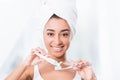 Beautiful african american young woman with towel wrapped over head putting toothpaste Royalty Free Stock Photo