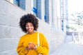 Beautiful African or American young woman walking in the street of the city looking at her phone smiling and having fun enjoying Royalty Free Stock Photo