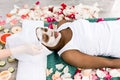 Beautiful african girl resting relaxing in spa resort with closed eyes while cosmetologist applies facial mask on her Royalty Free Stock Photo
