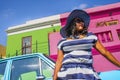 A beautiful African woman in a blue and white striped dress in front of a vintage Ford Cortina and traditional homes of Bo-Kaap, C