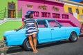 A beautiful African woman in a blue and white striped dress in front of a vintage Ford Cortina and traditional homes of Bo-Kaap, C
