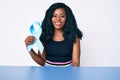 Beautiful african woman holding blue ribbon looking positive and happy standing and smiling with a confident smile showing teeth Royalty Free Stock Photo