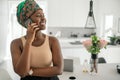 Black African woman home smiling, using smartphone, traditional headscarf Royalty Free Stock Photo