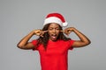Beautiful african woman in santa hat cover ears with finger of noice on grey background Royalty Free Stock Photo