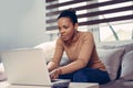 Beautiful african woman using laptop computer while sitting at a couch at home. Royalty Free Stock Photo