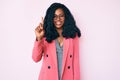 Beautiful african woman wearing business jacket and glasses showing and pointing up with finger number one while smiling confident Royalty Free Stock Photo