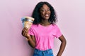 Beautiful african young woman holding canadian dollars looking positive and happy standing and smiling with a confident smile Royalty Free Stock Photo