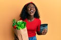 Beautiful african young woman holding groceries and calculator smiling and laughing hard out loud because funny crazy joke